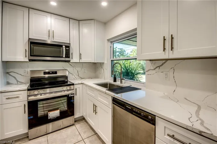 Kitchen featuring stainless steel appliances, white cabinets, light stone countertops, and light tile patterned floors