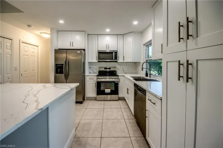 Kitchen with stainless steel appliances, light stone countertops, white cabinets, and recessed lighting