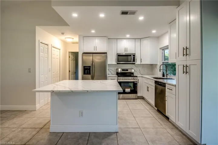 Kitchen with appliances with stainless steel finishes, light stone counters, white cabinetry, recessed lighting, and a kitchen island