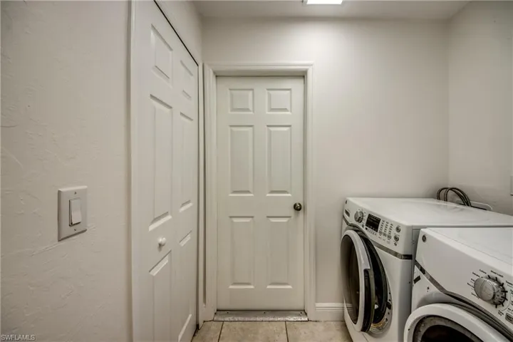 Laundry area with a textured wall, separate washer and dryer, and light tile patterned flooring