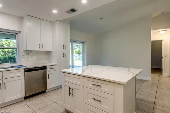 Kitchen featuring light tile patterned floors, dishwasher, white cabinetry, a kitchen island, and light stone counters