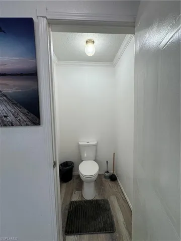 Water closet with toilet featuring wood finished floors, ornamental molding, and a textured ceiling