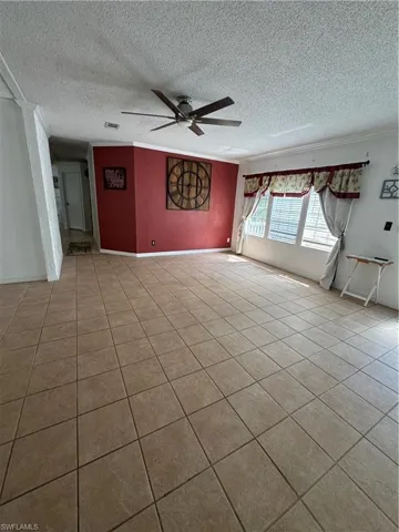 Hallway - Tiled empty room with ceiling fan, a textured ceiling, and ornamental molding