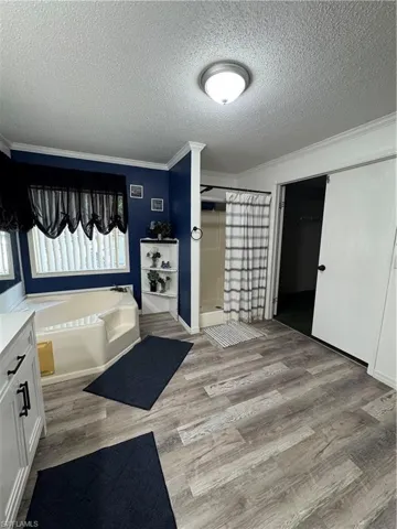 Master bathroom with a textured ceiling, ornamental molding, a shower stall, wood finished floors, and a bath