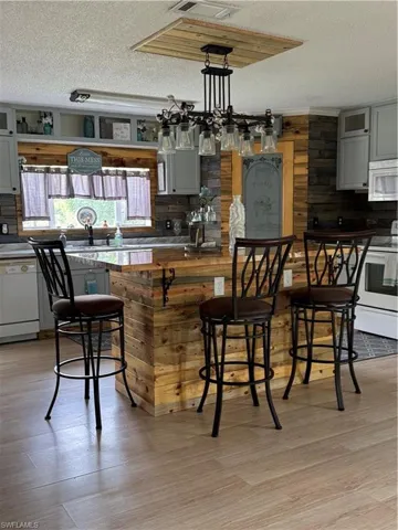 Kitchen with a textured ceiling, dishwashing machine, gray cabinets, decorative backsplash, and light wood-type flooring