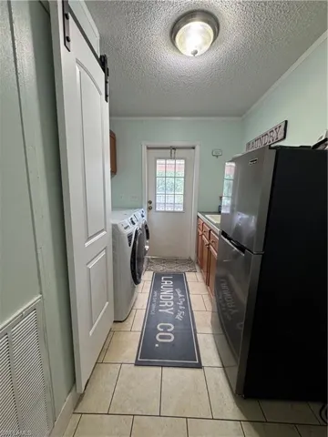 Washroom featuring cabinet space, washing machine and dryer, a textured ceiling, a barn door, and light tile patterned floors