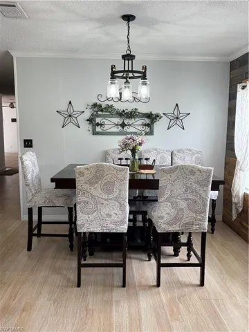 Dining area featuring crown molding, a chandelier, light wood-style flooring, and a textured ceiling
