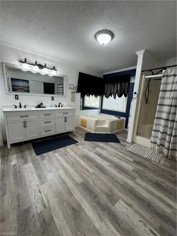 Bathroom featuring crown molding, a stall shower, a bath, a textured ceiling, and double vanity