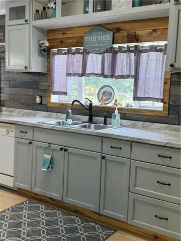 Kitchen with dishwashing machine, light stone counters, backsplash, and light wood-style flooring