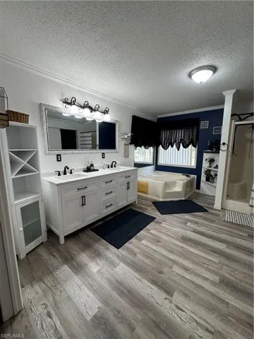 Master Bathroom featuring crown molding, a bath, a textured ceiling, double vanity, and wood finished floors