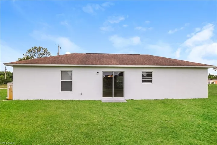 Rear view of house featuring stucco siding, a lawn, and roof with shingles
