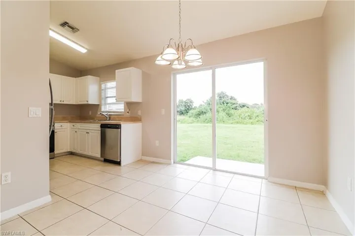 Kitchen with light countertops, suspended lighting, stainless steel dishwasher, white cabinets, and light tile patterned floors