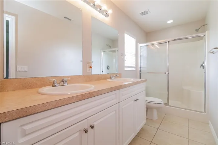 Bathroom featuring double vanity, a stall shower, and light tile patterned flooring