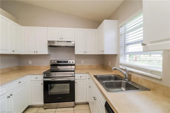 Kitchen with stainless steel electric range oven, white cabinetry, light countertops, vaulted ceiling, and light tile patterned floors