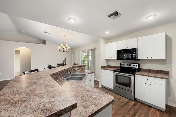 Kitchen with stainless steel electric stove, white cabinets, sink, dark hardwood / wood-style floors, and a kitchen island with sink