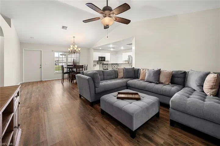 Living room with lofted ceiling, dark hardwood / wood-style flooring, and ceiling fan with notable chandelier