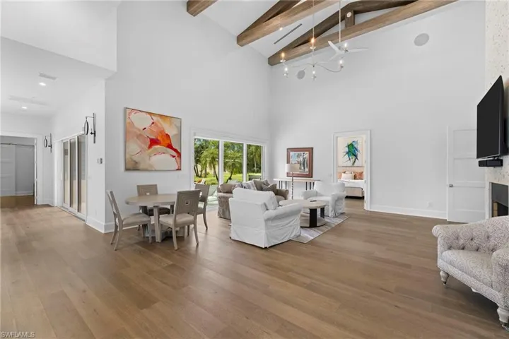 Living room featuring light wood finished floors, a chandelier, a high ceiling, and beam ceiling