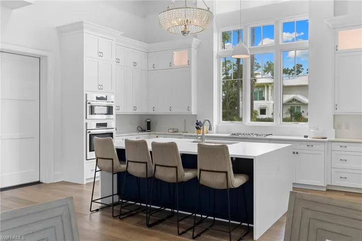 Kitchen with a towering ceiling, a center island with sink, light stone counters, light wood finished floors, and a breakfast bar area