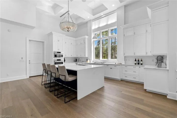 Kitchen with a kitchen island with sink, a chandelier, white cabinets, a kitchen breakfast bar, and a towering ceiling
