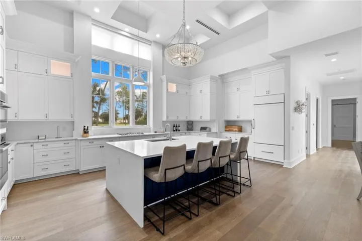 Kitchen with white cabinetry, light stone counters, dark wood-style flooring, a center island with sink, and hanging light fixtures