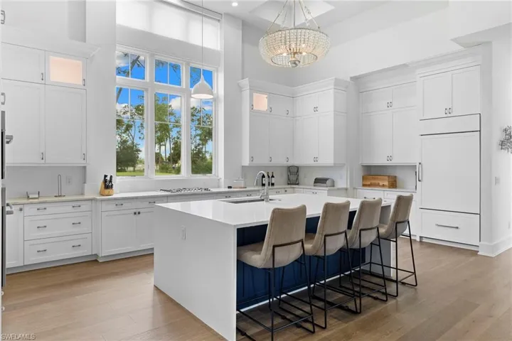 Kitchen featuring white cabinetry, light wood-type flooring, light stone counters, a center island with sink, and a high ceiling