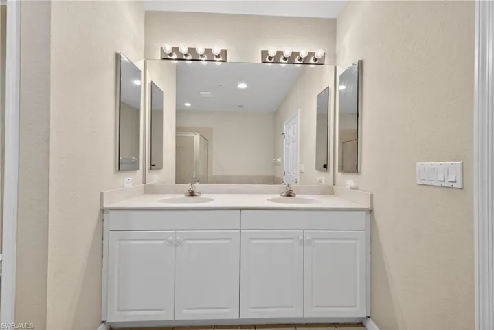 Bathroom featuring a textured wall, double vanity, and a shower stall