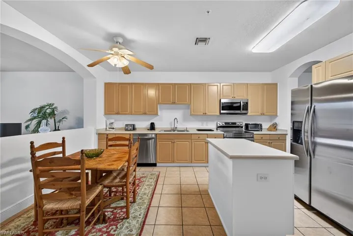 Kitchen featuring New stainless steel Stove, Microwave, dishwasher, arched walkways, light countertops, and light tile patterned floors