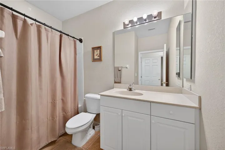 Bathroom with a textured wall, vanity, shower / bath combination with curtain, and light tile patterned floors