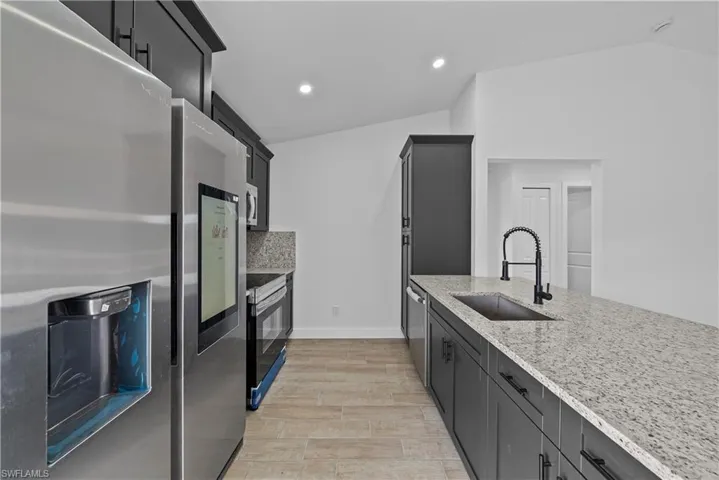 Kitchen with stainless steel appliances, light stone counters, lofted ceiling, wood finish floors, and recessed lighting