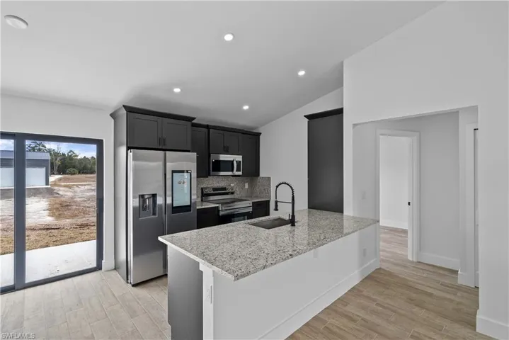 Kitchen featuring stainless steel appliances, light wood-style flooring, light stone counters, lofted ceiling, and tasteful backsplash