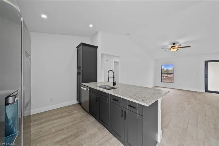 Kitchen with light stone countertops, stainless steel appliances, light wood-style floors, ceiling fan, and vaulted ceiling
