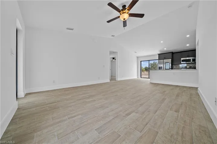 Unfurnished living room featuring wood finish floors, a ceiling fan, vaulted ceiling, and recessed lighting