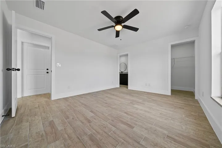 Unfurnished bedroom featuring wood finish floors, a walk in closet, a ceiling fan, and ensuite bath