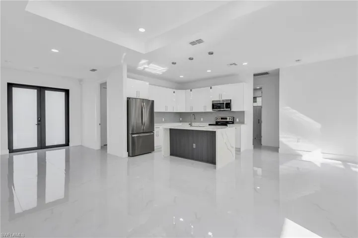 Kitchen with a kitchen island with sink, white cabinets, hanging light fixtures, backsplash, and appliances with stainless steel finishes