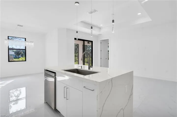 Kitchen featuring pendant lighting, sink, a center island with sink, white cabinetry, and light stone countertops
