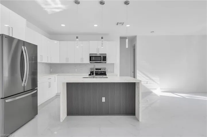 Kitchen featuring a center island with sink, pendant lighting, stainless steel appliances, and white cabinets