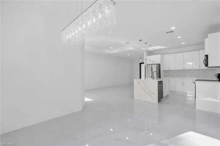 Kitchen with hanging light fixtures, light stone counters, white cabinets, black appliances, and a chandelier