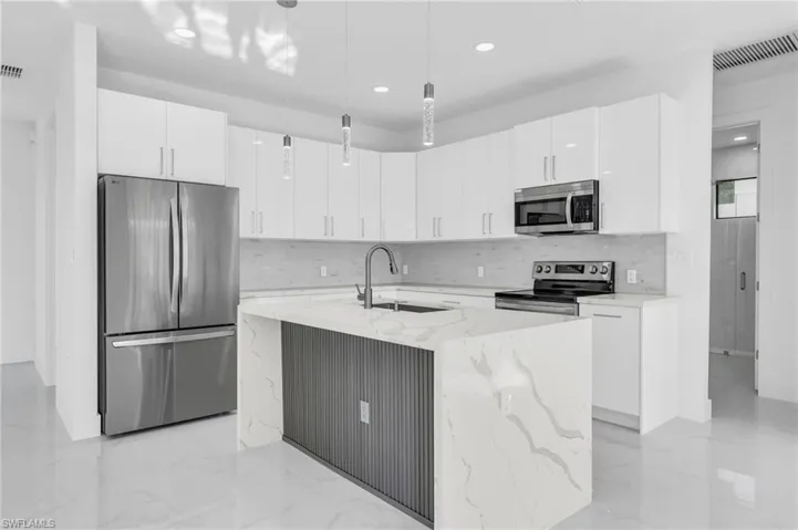 Kitchen featuring pendant lighting, a kitchen island with sink, appliances with stainless steel finishes, and white cabinetry