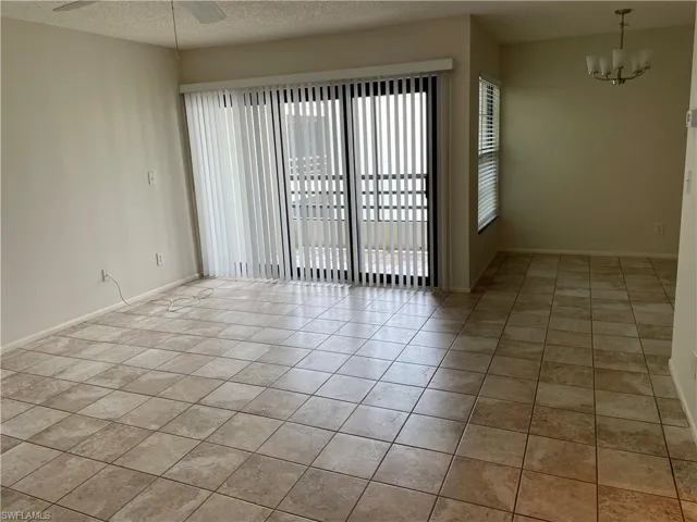 Empty room with tile patterned flooring, ceiling fan with notable chandelier, and a textured ceiling