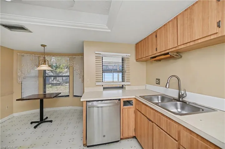 Kitchen featuring dishwasher, light countertops, decorative light fixtures, and light brown cabinetry