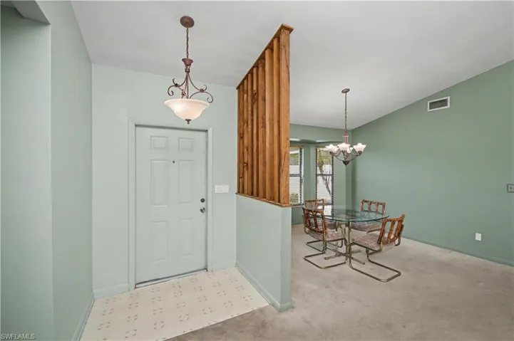 Foyer entrance with carpet flooring, vaulted ceiling, and a chandelier