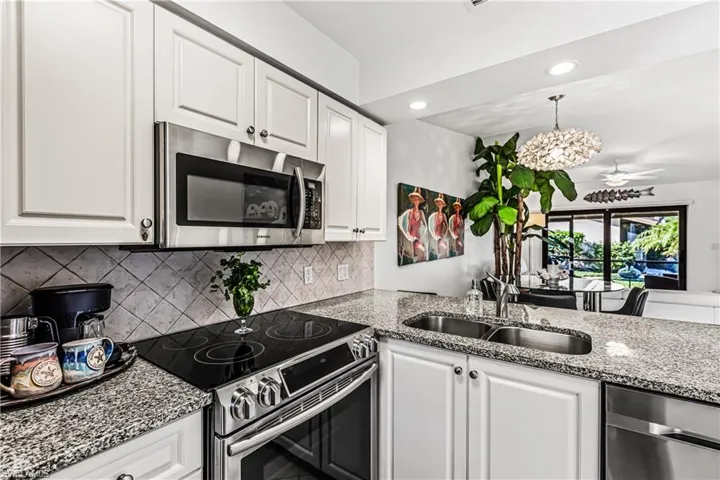 Kitchen featuring light stone counters, stainless steel appliances, white cabinetry, and ceiling fan