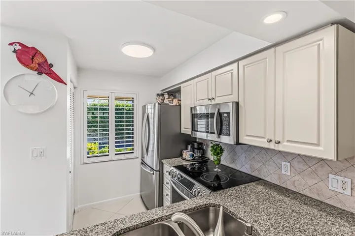 Kitchen with stainless steel appliances, dark stone countertops, backsplash, and light tile patterned floors