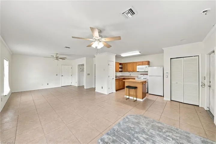 Open-concept interior featuring large-format tile flooring, dual ceiling fans, wood cabinetry, and a kitchen island