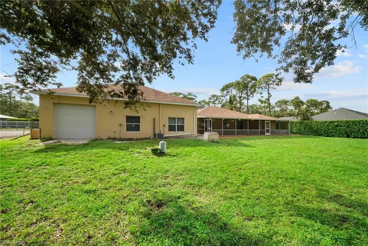 Expansive backyard featuring a large grass lawn, mature trees, a screened-in rear porch, and a detached single-car garage