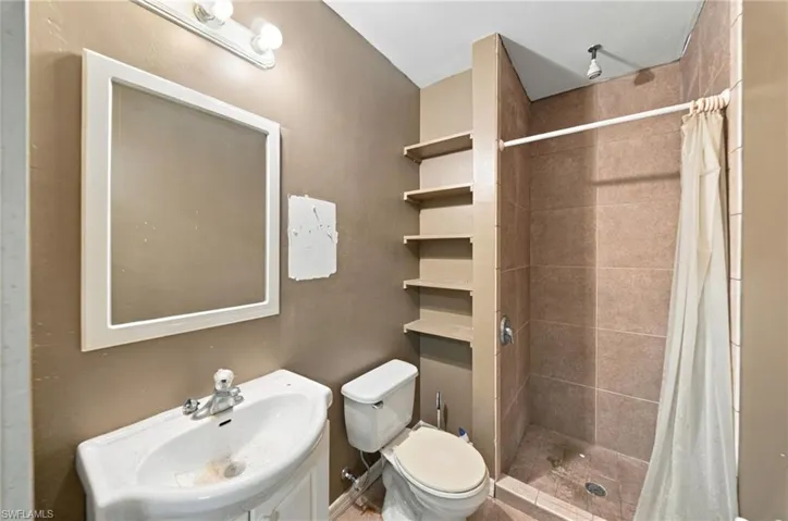 Bathroom featuring a pedestal sink, wall-mounted mirror with white frame, multi-level built-in shelving, and a tiled shower stall