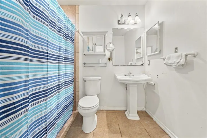 Pedestal sink, wall-mounted medicine cabinet, rectangular vanity mirror, three-light fixture, and tiled flooring