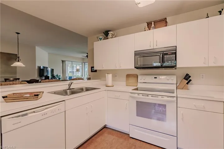 Kitchen featuring white cabinets, light hardwood / wood-style floors, decorative light fixtures, sink, and white appliances