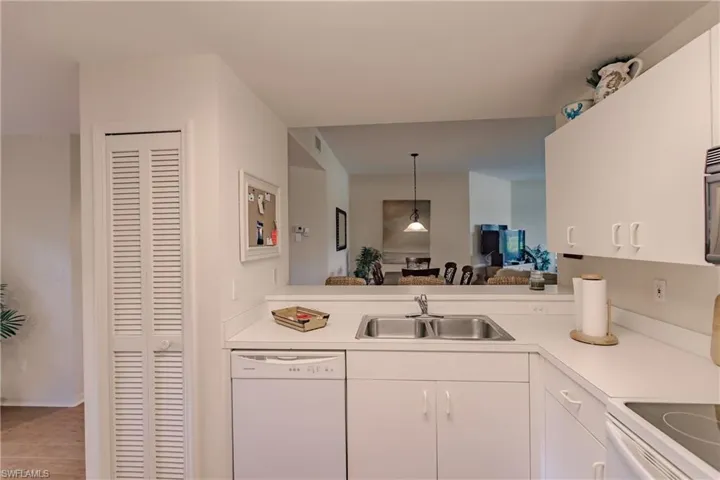 Kitchen with white appliances, sink, light wood-type flooring, pendant lighting, and white cabinets