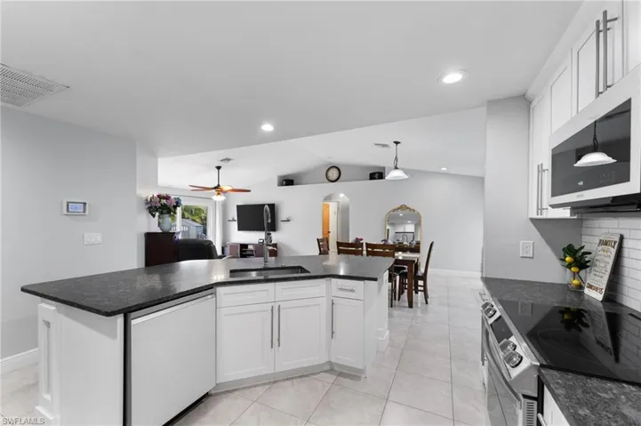 Kitchen featuring a center island, appliances with stainless steel finishes, white cabinetry, hanging light fixtures, and vaulted ceiling